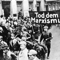 Nazi parade features a banner proclaiming, “Death to Marxism.”The possibility of a peaceful Germany after World War I was precluded entirely by the terms of the Versailles Treaty and the intransigent hostility of France and England. Stripped of industries and sources of raw materials, and saddled with impossible reparations payments, Germany was split drastically between extremists of left and right. The government at Weimar was held responsible for the political and economic chaos, and its inability to placate internal and external enemies practically assured a radical turn in politics.