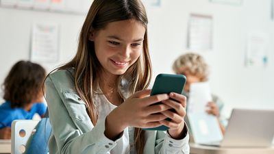 Happy Hispanic girl looking at smartphone in classroom. student, cellphone, smart phone, education, cell phone bans in school
