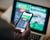 A sports bettor looks at their phone; the game is on TV in the background.