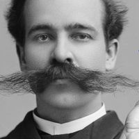 A black-and-white photo of a white man from the late 19th century wearing an extremely long mustache. Cut-out hands hold a blue razor to the right side of the image.
